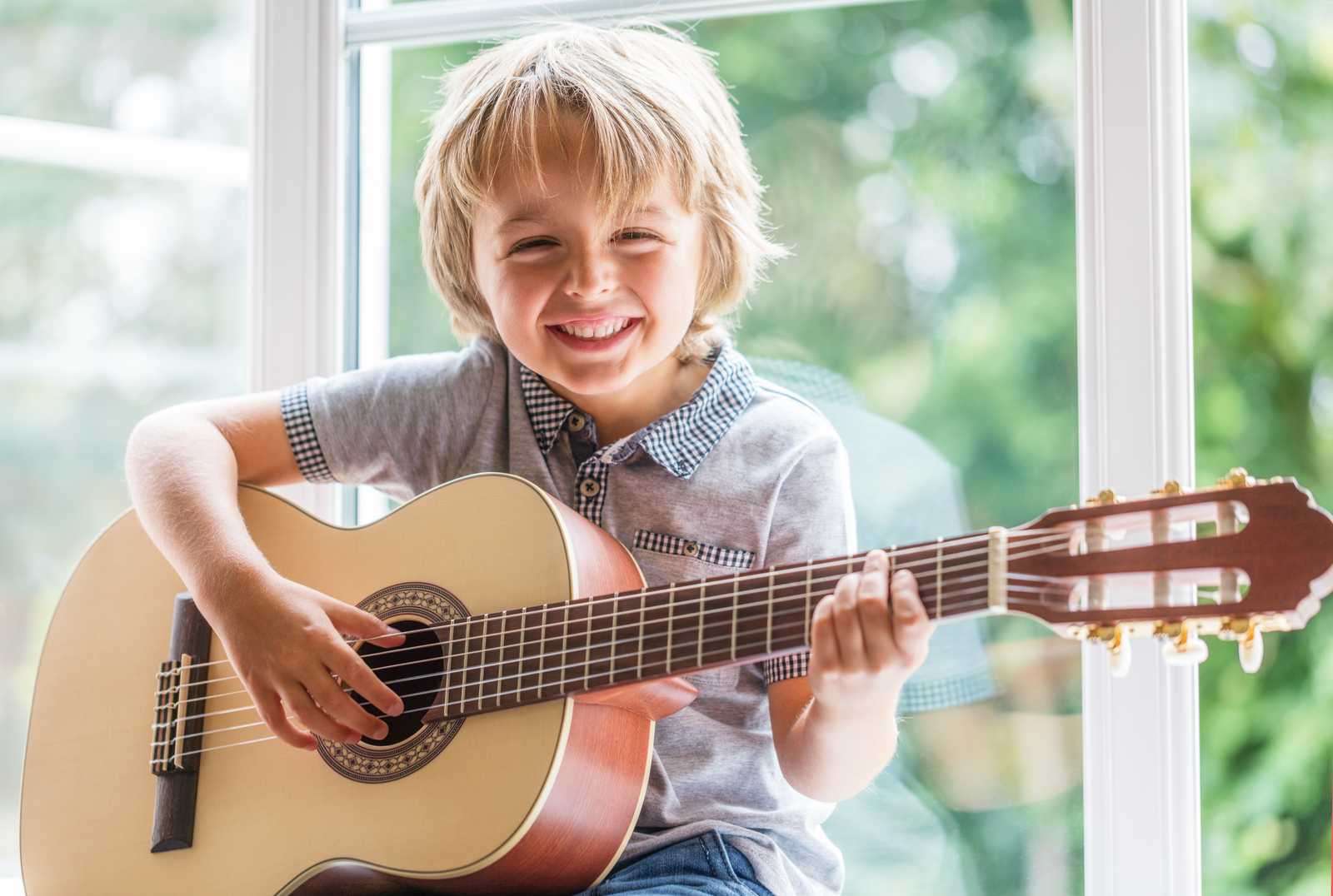 a young boy smiling and holding the guitar
