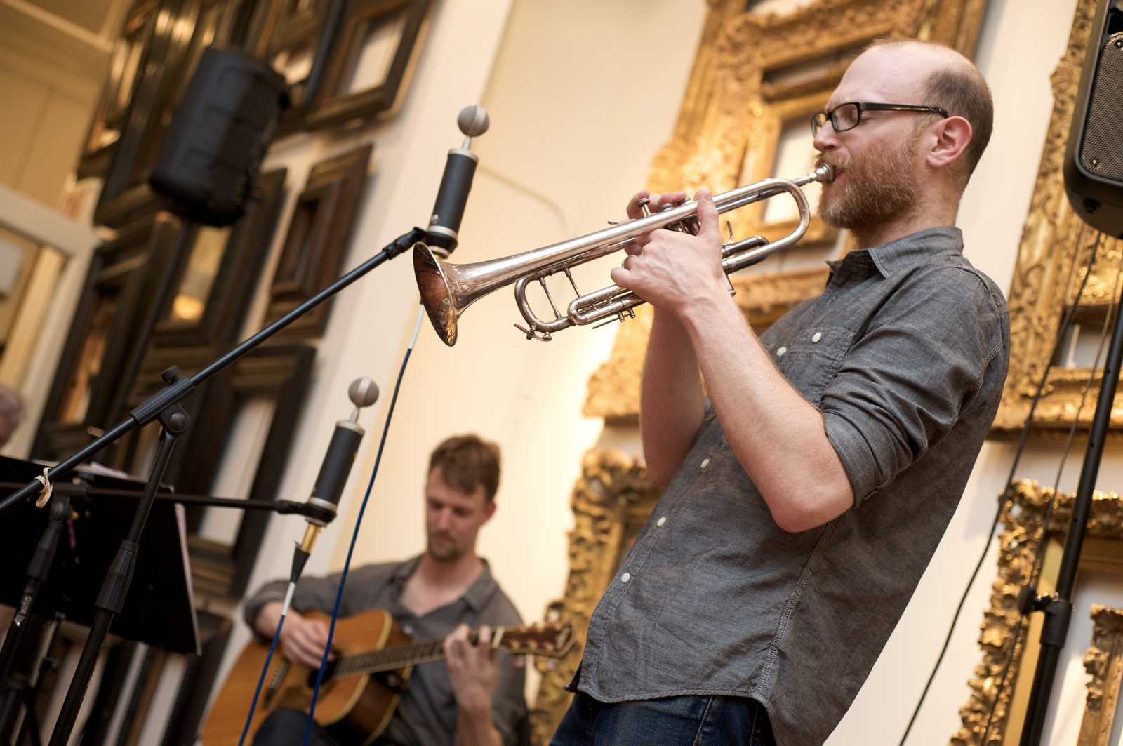 A man performing on the trumpet accompanied by a guitarist