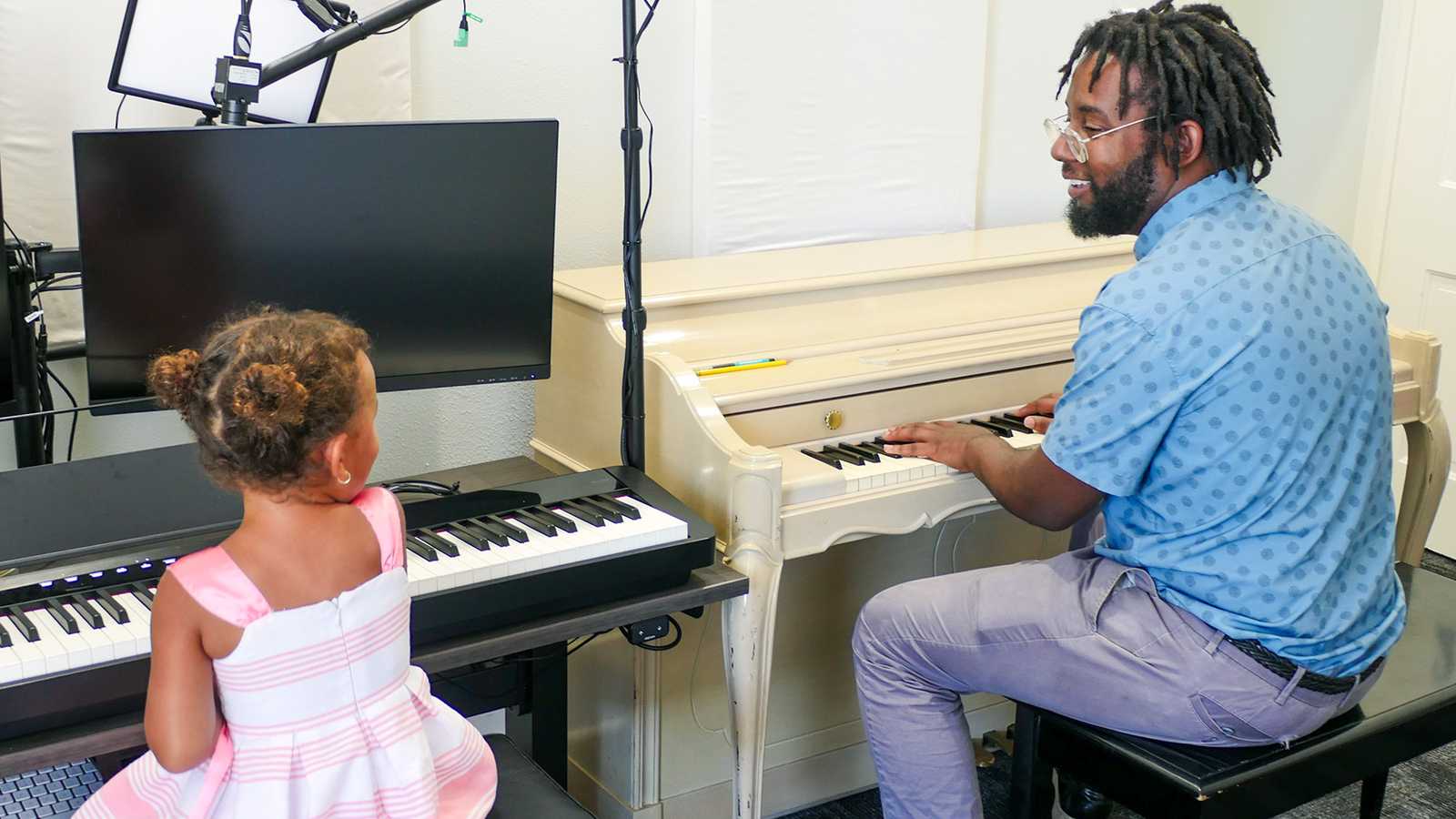 A man giving a piano lesson to a young girl